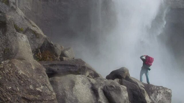 a hiker observes a waterfall on an overcast day