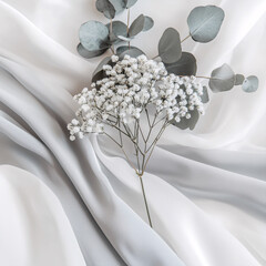 Delicate baby's breath and eucalyptus sprigs rest on softly draped white fabric, creating a serene and minimalist composition.
