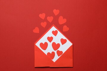 Valentine's Day. Envelope with many paper hearts on red background, top view