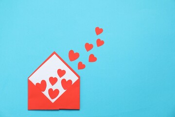 Valentine's Day. Envelope with many paper hearts on light blue background, top view. Space for text