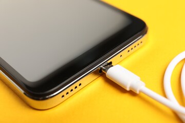 USB charge cable connected to smartphone on orange background, closeup