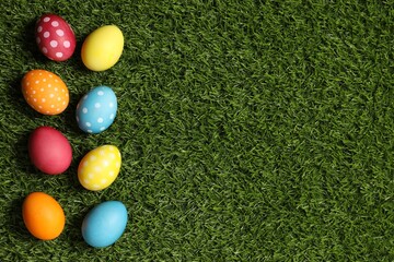 Naklejka premium Beautiful decorated Easter eggs on green grass, flat lay. Space for text