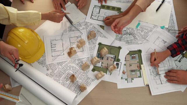 Architect and safety engineer discussion about building construction use blueprint on table with architectural document, measurement tool and wooden block scatter around at modern office. Delineation.