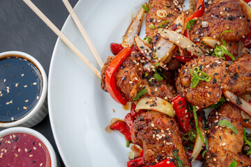 Chicken wings marinated and fried in sweet soy sauce with plated peppers and onions, soy sauces and sweet and sour sauce on the side with rashi-type cutlery on top.