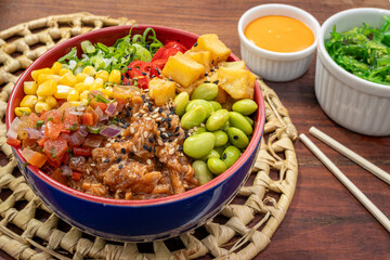  shredded pork poke, gyoza serving as the base for the poke, Diced mango, or green soybeans, Black sesame seeds, vinaigrette, corn and chives , served in a ceramic bowl placed on a locked straw mat.