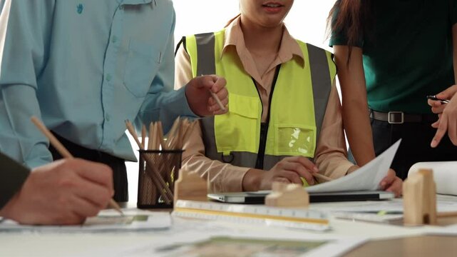 Smart architect and safety engineer discussion about building blueprint on table with architectural document, measurement tools and wooden block scatter around at modern office. Closeup. Delineation.