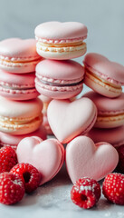 Fototapeta premium Delicate pink heart-shaped macarons stacked with fresh strawberries and raspberries on a marble surface