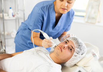 Experienced female cosmetic doctor carefully performs procedure on her male patient using...