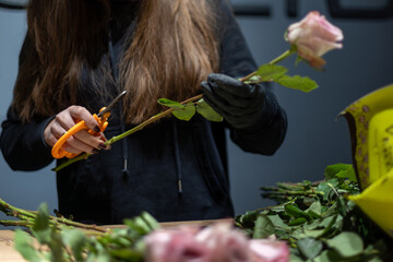 Florist trimming a pink rose with orange pruning shears, close-up of hands and tools.