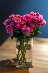 Elegant bouquet of pink roses in a glass vase with water, placed on a wooden table.