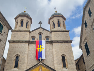Kotor, Montenegro - July 2, 2024: Old historic downtown. Saint Nicholas Church towers against blue cloudscape. Colorful banner above entrance pediment