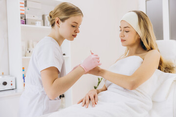Fototapeta premium Professional beautician carefully applying cosmetics on a young woman's hand during a skin care treatment session in a modern beauty salon