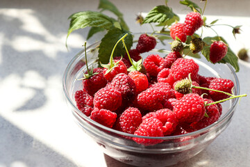 Ripe raspberries in a glass bowl on the kitchen table, close-up
