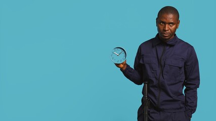 Security guard holding clock, rushing people out of property, isolated over studio backdrop. Man in...