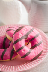 Sweet pink donut with chocolate strips on plate on kitchen table.