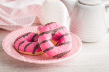 Sweet pink donut with chocolate strips on plate on kitchen table.