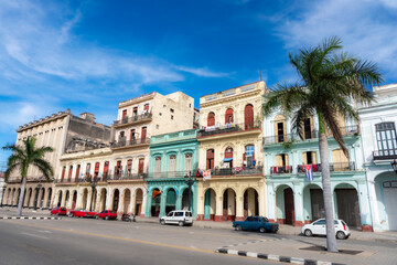 Vibrant colonial-style buildings with balconies in Havana, Cuba, featuring pastel colors, palm trees, and classic cars parked along the street.