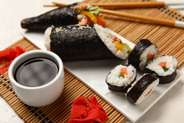 Bamboo mat with tasty sushi rolls, ginger and soy sauce on light table, closeup