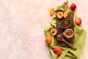 Wooden board with bowl and jar of sweet apricot jam on pink background