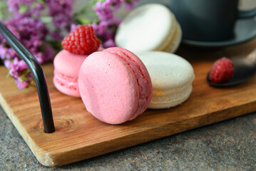 Wooden tray with sweet macaroons and raspberries on dark background