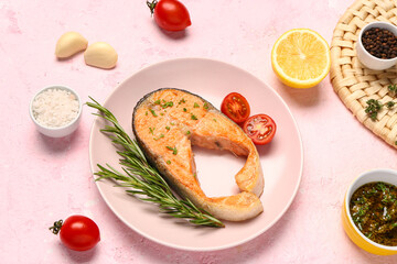 Plate of tasty salmon steak with tomatoes and lemon on pink background