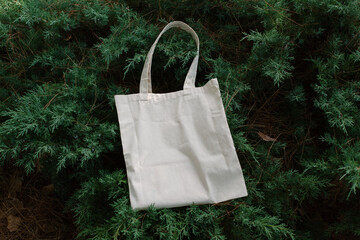 White cotton or mesh bag on green branches of a coniferous bush background. Zero waste, no plastic,...