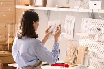 Female jewelry designer with sketch of stylish accessory at workplace