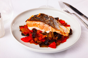 Salmon steak with stewed vegetables, eggplants and tomatoes, served on table, over white background.