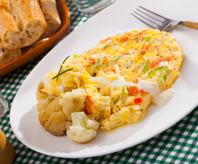 Tasty omelet with vegetables served with baked cauliflower and delicate cheese sauce..