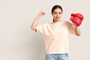 Naklejka premium Young woman with boxing gloves flexing muscles on white background. Feminism concept