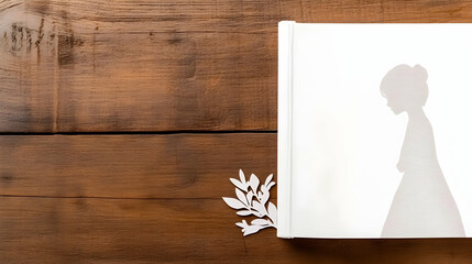 White book with girl silhouette and leaves on wood.