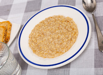 Boiled oatmeal porridge served in white plate. Concept of diet food