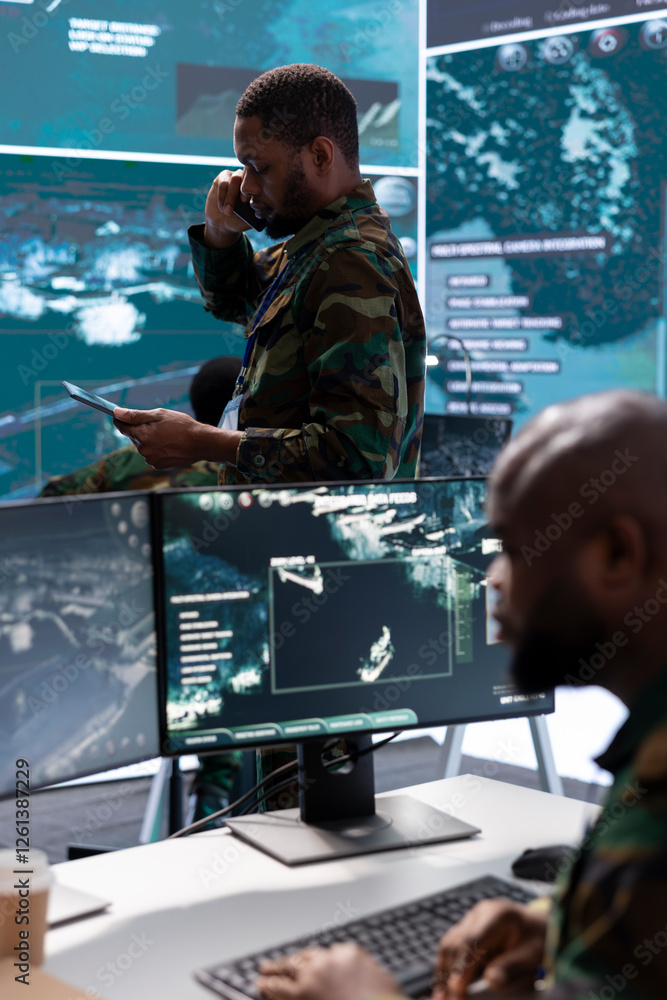 Poster soldier discussing on phone call in a modern control room, processing real time data and coordinatin