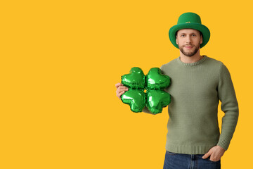 Young man in leprechaun hat with air balloon in shape of clover on yellow background. St. Patrick's...