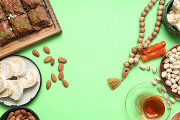 Composition with traditional Eastern sweets, tea and tasbih for Ramadan on green background