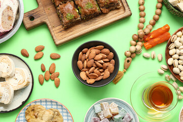 Composition with different Eastern sweets, tea and tasbih for Ramadan on green background