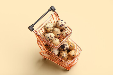 Shopping cart with fresh quail eggs on beige background