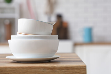 Stack of white clean tableware on wooden table in kitchen