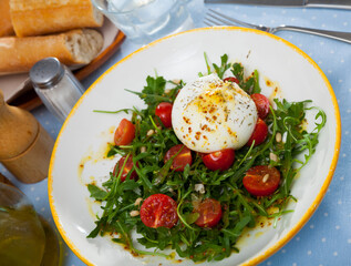 Close up of salad with burrata cheese, pine nuts, cherry tomatoes and arugula with spice at plate