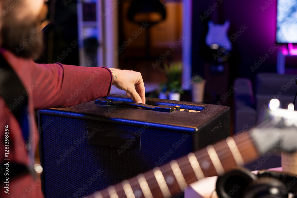 Poster sound engineer adjusting volume levels on his amplifier to record acoustic guitar tunes for editing 
