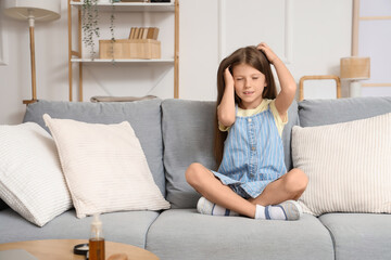 Little girl with pediculosis scratching her head on sofa at home