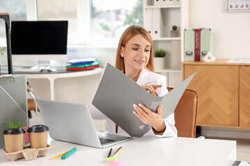 Young businesswoman working with document folder at table in office