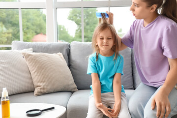 Mother combing her little daughter's hair with pediculosis on sofa at home