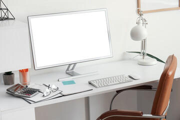 Workplace with blank computer monitor and lamp in light office