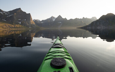 A green sea kayak on a mirror flat ocean surrounded by mountains at sunset in Norway. 