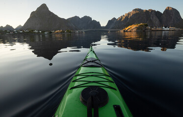 Sunset sea kayaking on a glassy ocean surrounded by mountains in Norway. 