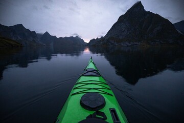 A sea kayak on a glassy lake at dusk and surrounded by mountains. 