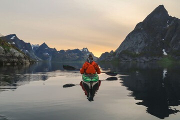 A sea kayaker in the middle of a fjord surrounded by mountains at sunset. 