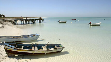 Fototapeta premium Tranquil beach scene boats on calm turquoise water near a pier, distant figures walking, clear sky