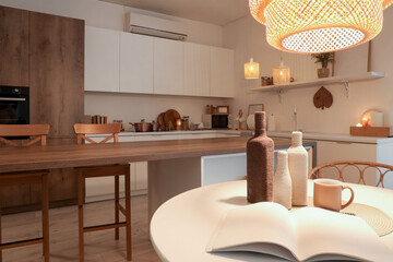 Interior of kitchen with dining table, counters and glowing lamps in evening
